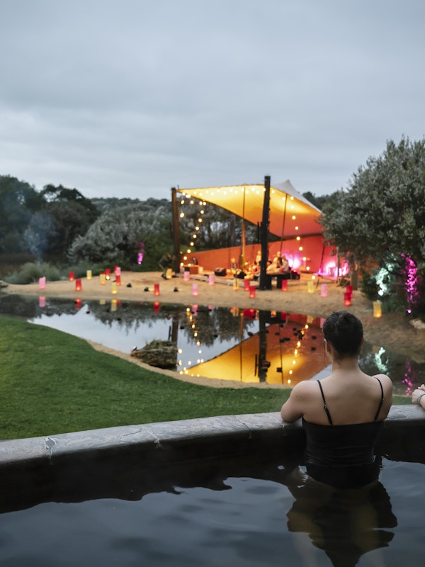 two girls sitting in a pool looking at a stage with fairy lights all around