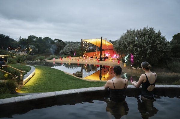 two girls sitting in a pool looking at a stage with fairy lights all around