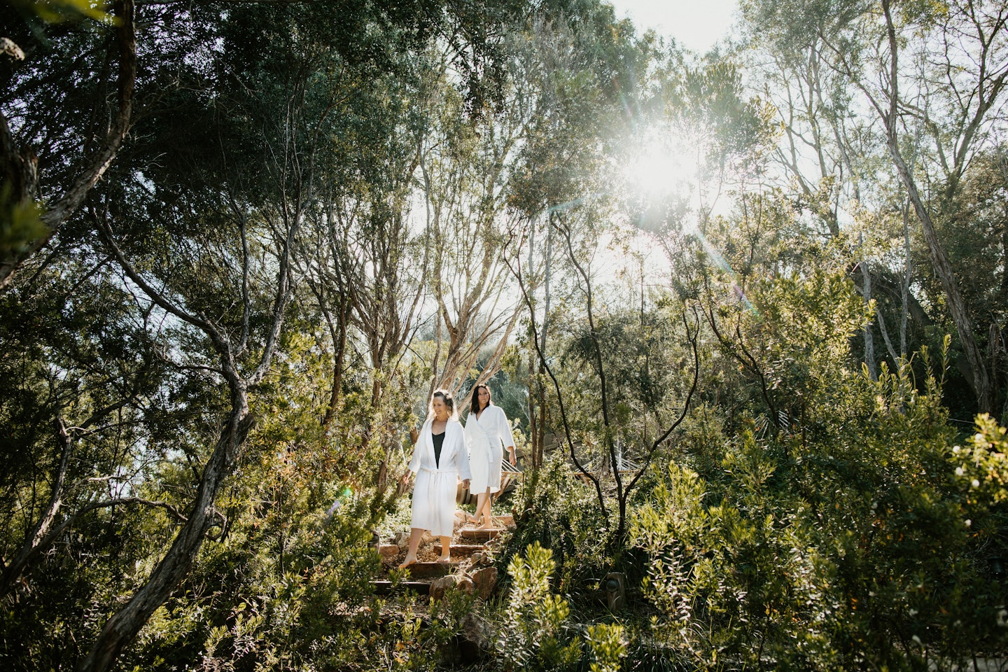 two women walking through nature in white robes