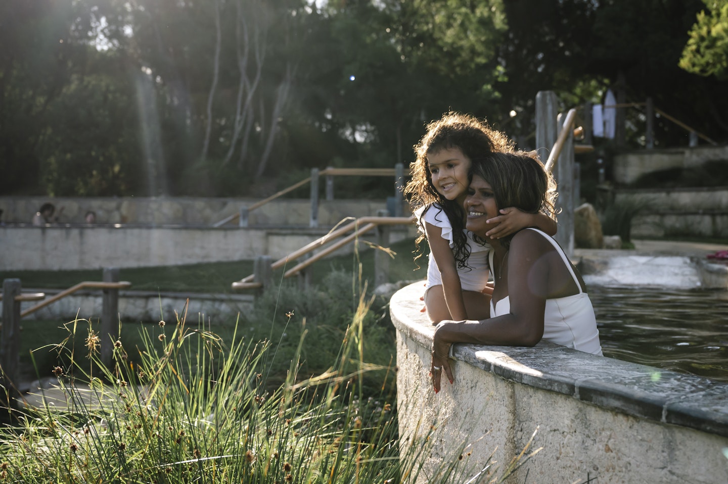 a mum and daughter sitting on the edge of an amphitheatre pool