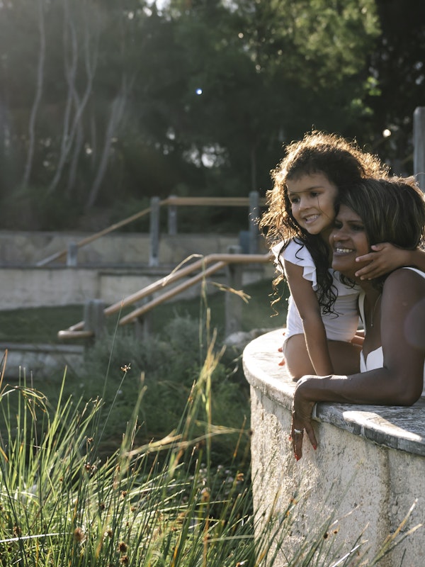 a mum and daughter sitting on the edge of an amphitheatre pool