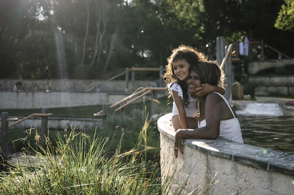 a mum and daughter sitting on the edge of an amphitheatre pool