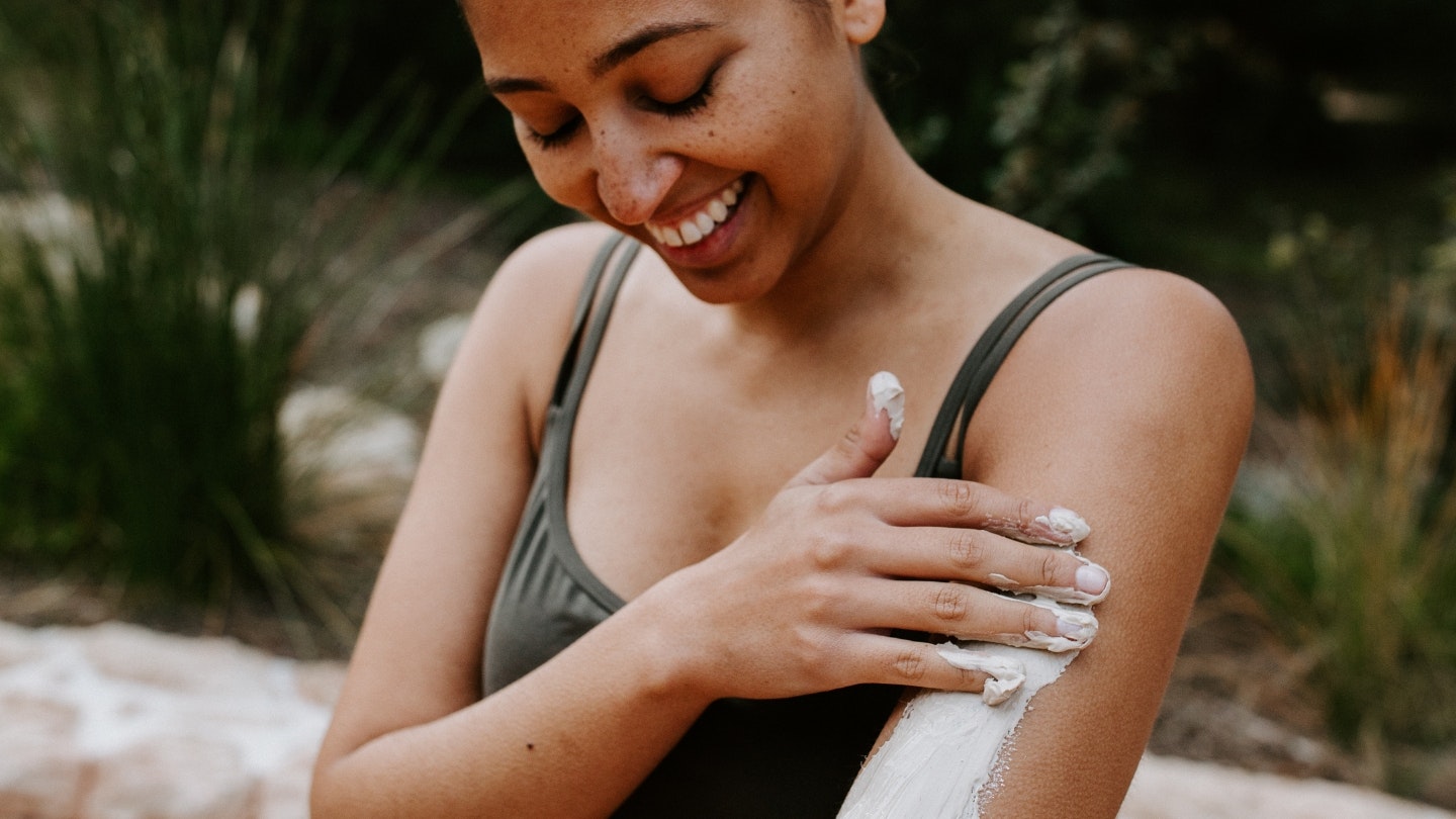 A woman applying body clay to her arm while smiling