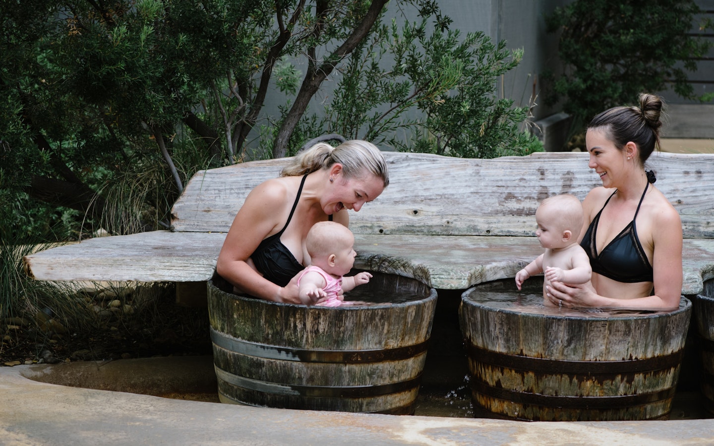 two women bathing in barrels with their babies