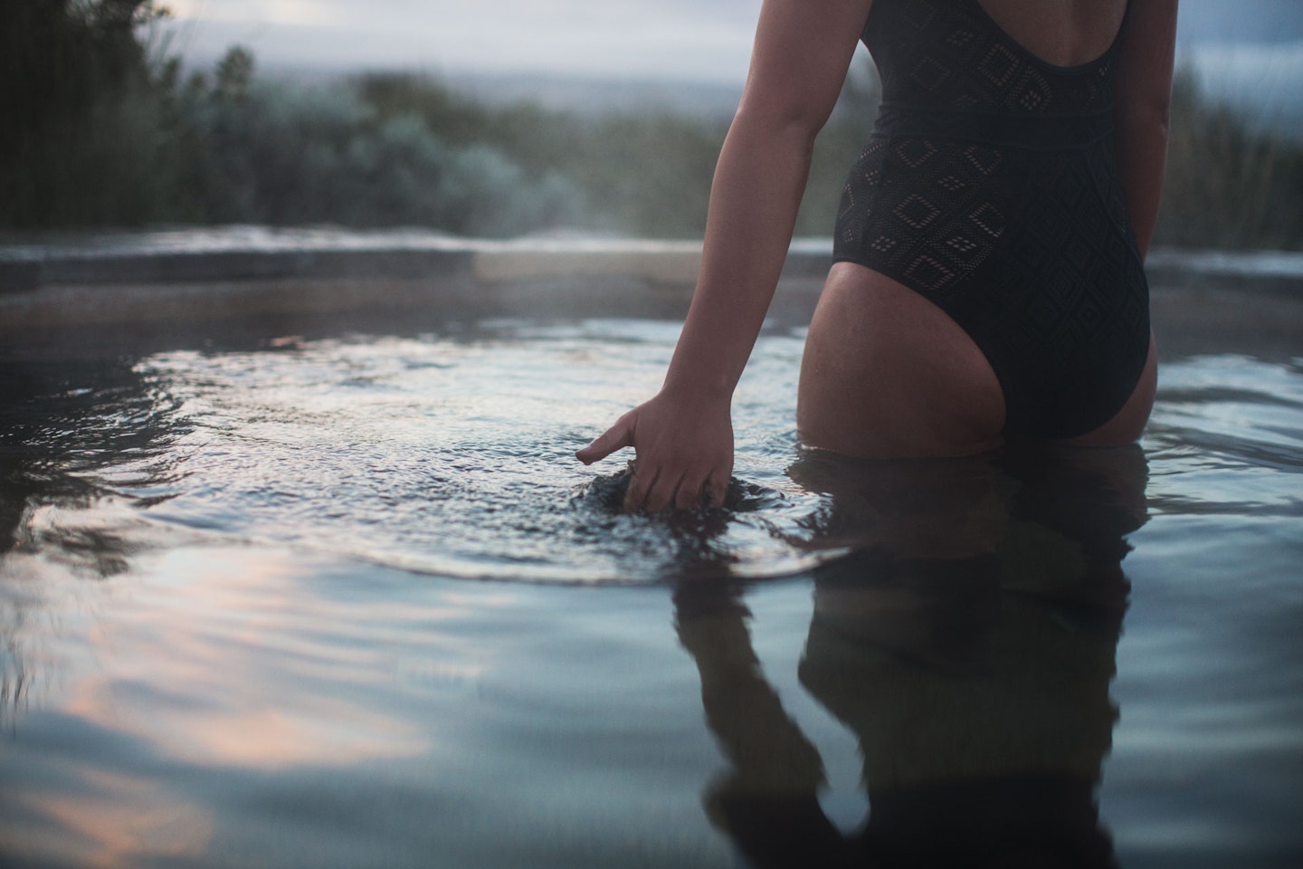 A woman skimming her hand along the surface of geothermal water