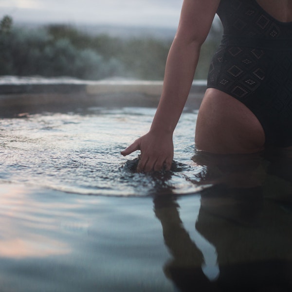 A woman skimming her hand along the surface of geothermal water