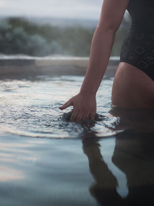 A woman skimming her hand along the surface of geothermal water