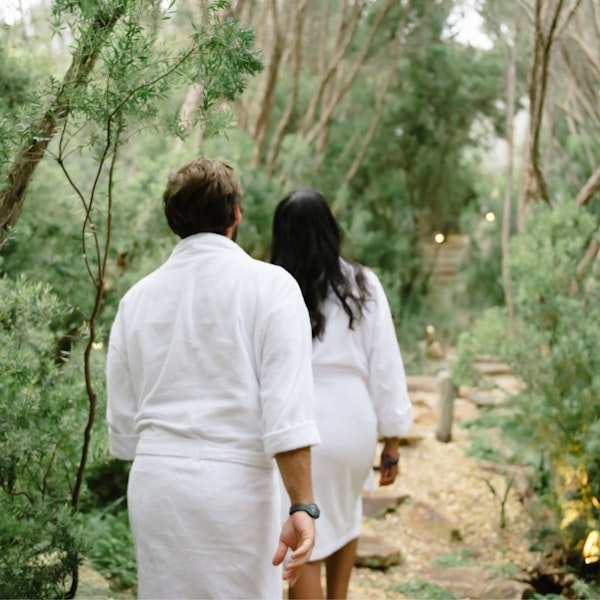 Two people walking through nature in white robes