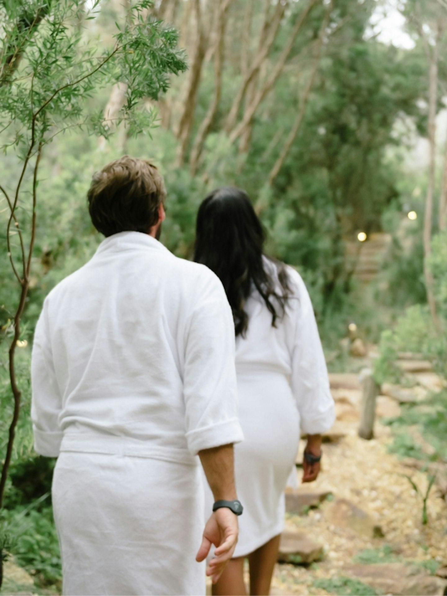 Two people walking through nature in white robes