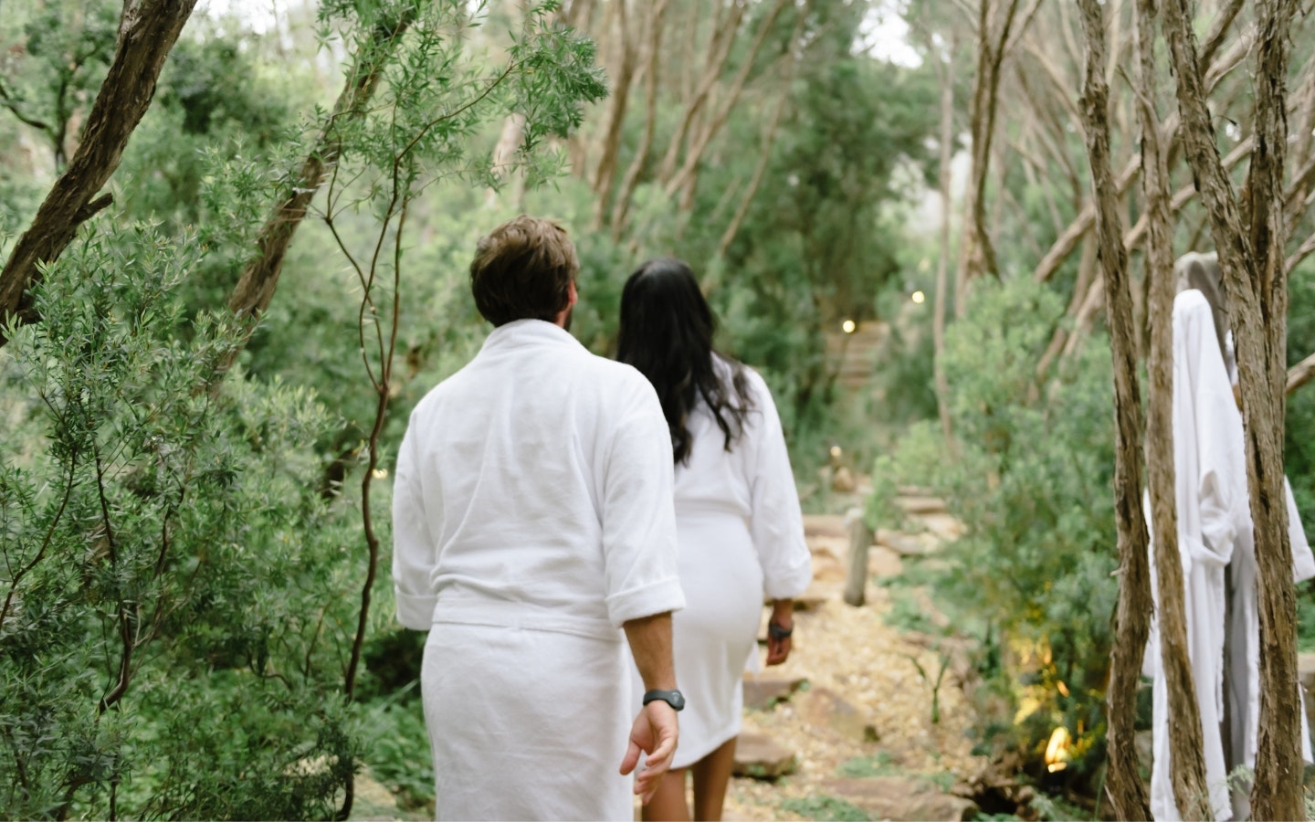 Two people walking through nature in white robes