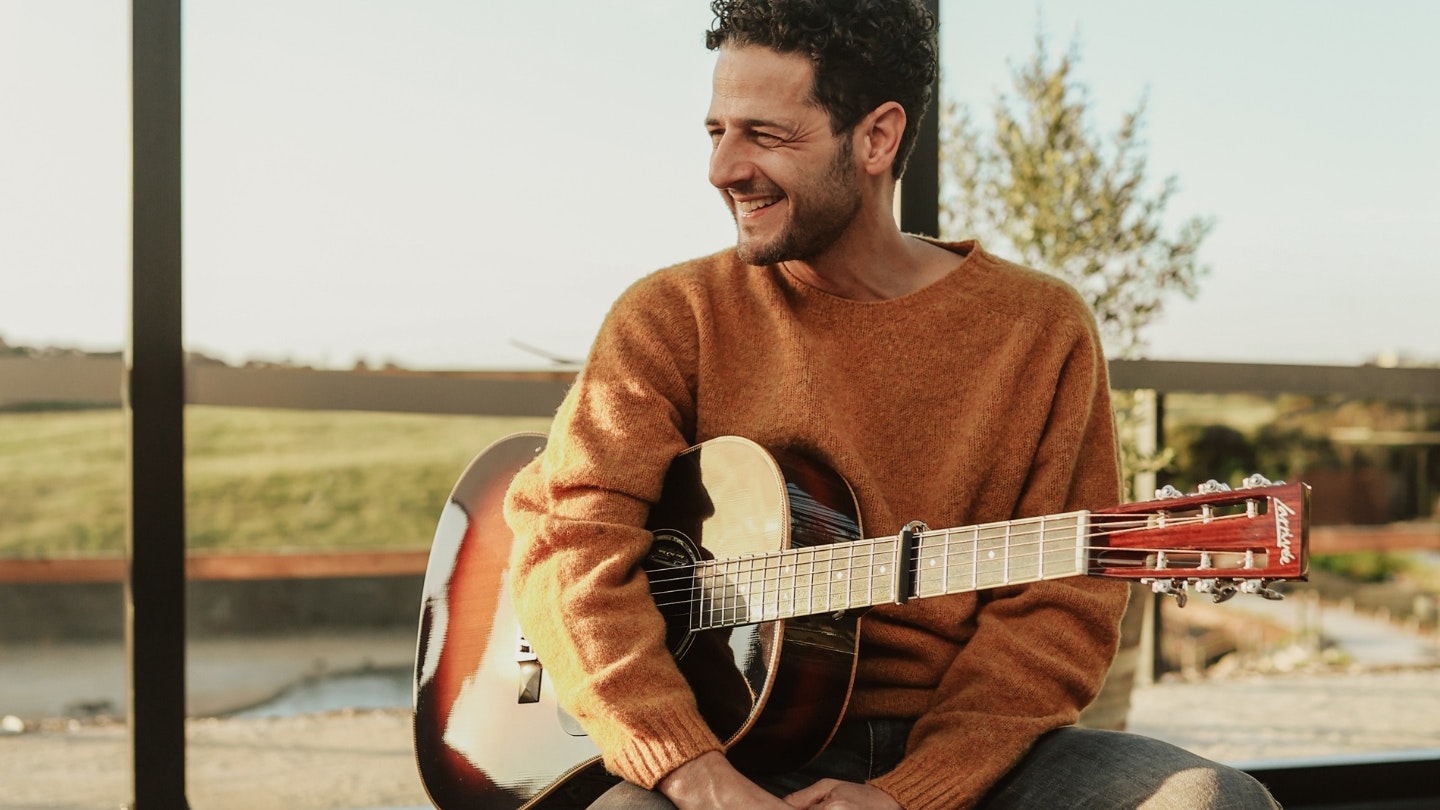 Lior: A man sitting on a stool laughing with a guitar in his hand