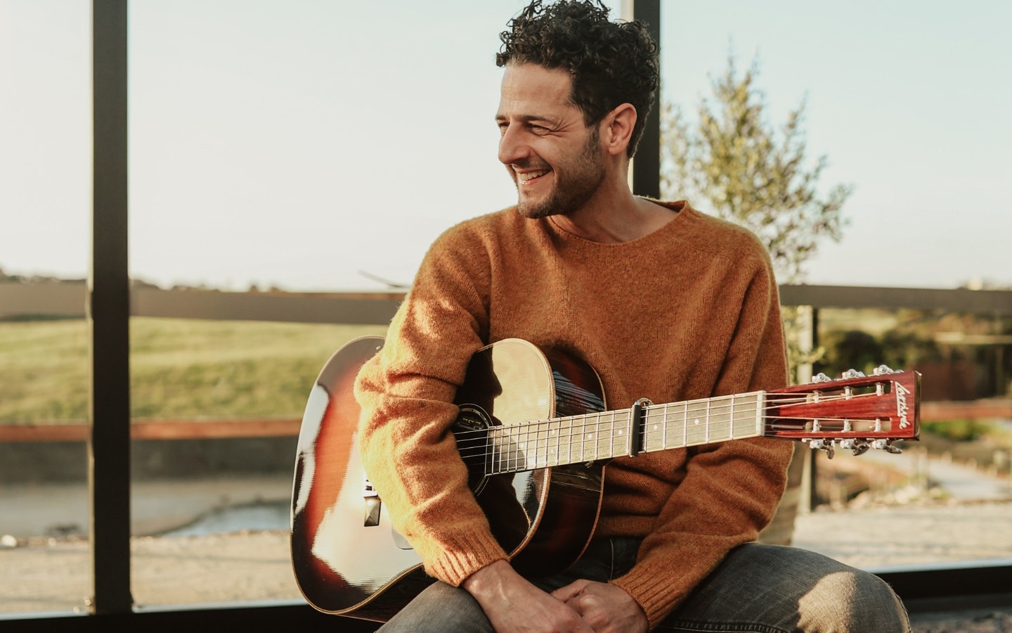 Lior: A man sitting on a stool laughing with a guitar in his hand