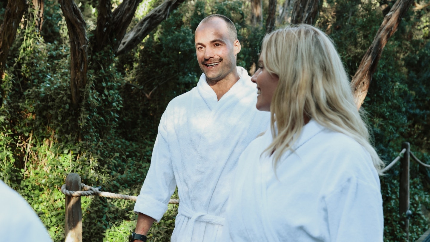 A young man and woman walking through nature in white robes at Peninsula Hot Springs