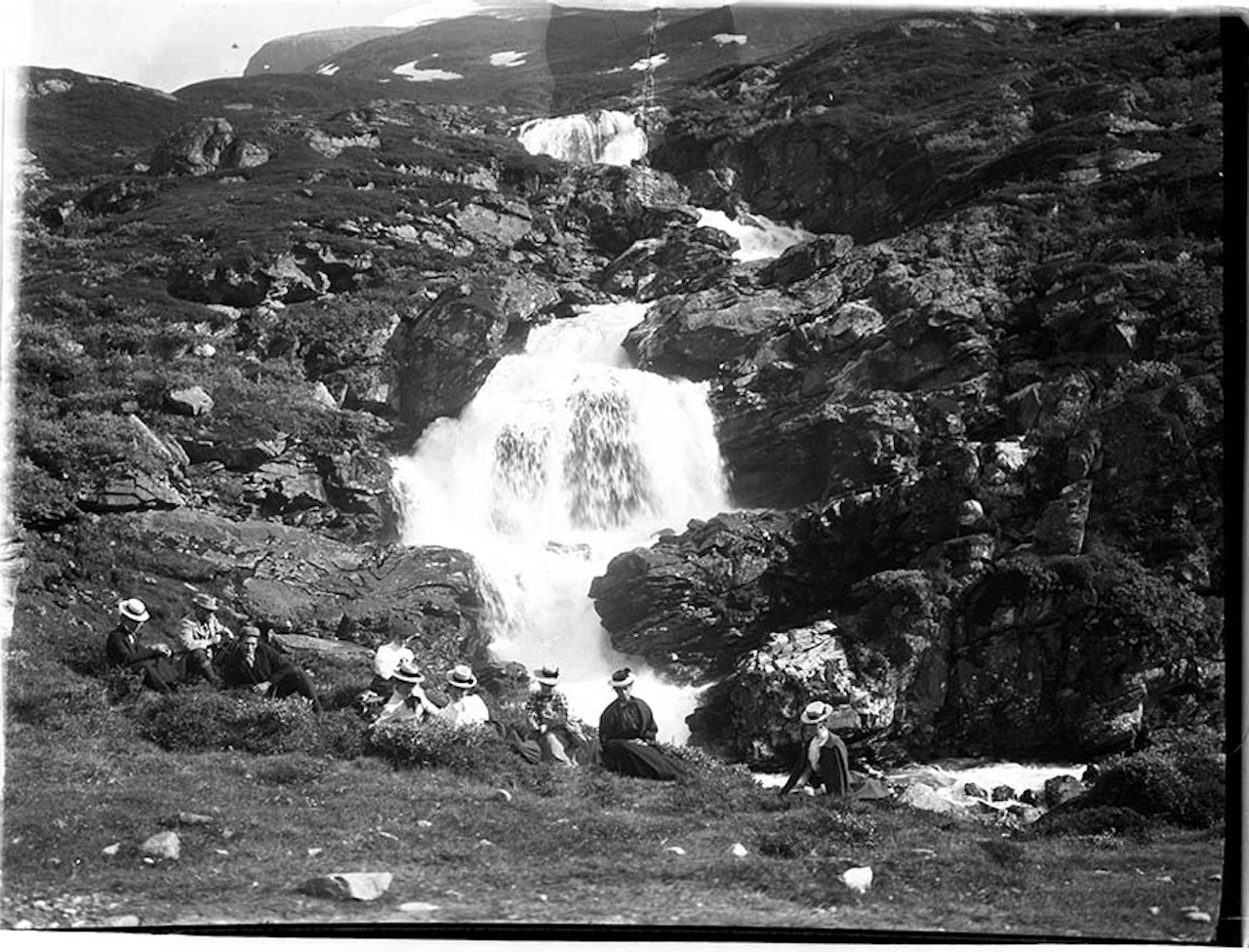 VED FOSSEN I SKAGADALEN: Therese Bertheau sitter midt i bildet, sortkledt. I venstre kant sitter Slingsby med lys jakke. Den unge mannen i forgrunnen er fjellføreren Elias Hogrenning. Foto er tatt av Howard Priestmann i 1900. Foto: Fra samlingen til Fjellmuseet i Lom therese bertheau utemagasinet