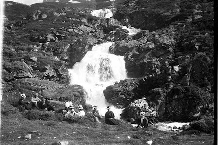 VED FOSSEN I SKAGADALEN: Therese Bertheau sitter midt i bildet, sortkledt. I venstre kant sitter Slingsby med lys jakke. Den unge mannen i forgrunnen er fjellføreren Elias Hogrenning. Foto er tatt av Howard Priestmann i 1900. Foto: Fra samlingen til Fjellmuseet i Lom therese bertheau utemagasinet