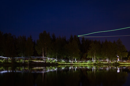 LYS I MØRKET: Hodelyktene danner kunstneriske striper langs vannkanten. Fra luften filmer en drone løperne.