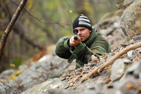 Jeger som sikter mot kamera med rifle og riflekikkert med retikkel