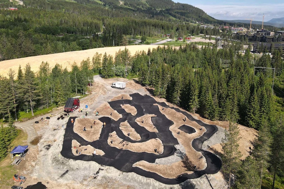 STOR: Man trenger ikke fyrstikkeske for å skjønne skalaen på den nye pumptracken i Trysil. I bakgrunnen ser du snø som ligger dekket av sagflis til vinteraktivitetene, og resten av anlegget. Foto: Bike Solutions. pumptrack trysil bike arena
