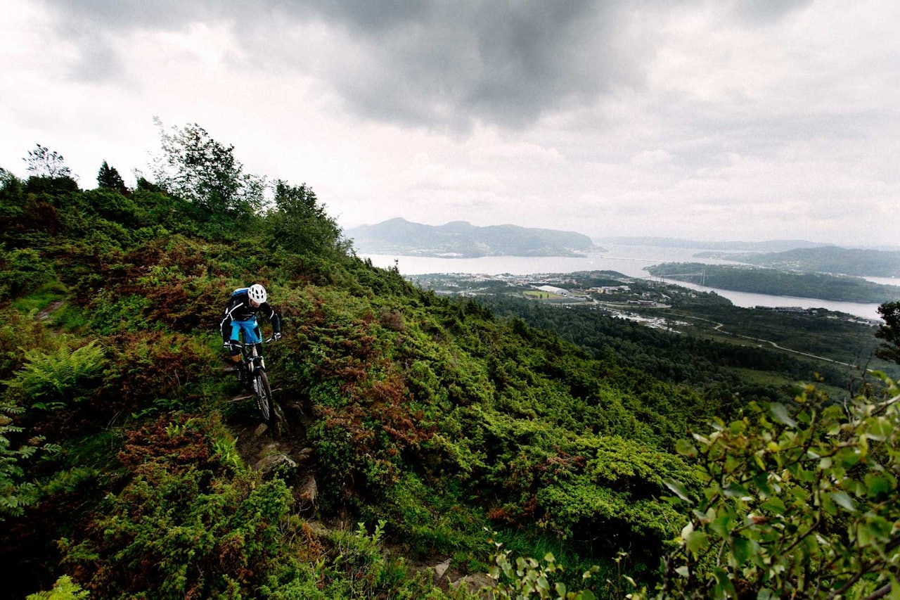 Bendik Been nyter utsikten over Knarvik et lite øyeblikk før stien forsvinner under tregrensa igjen. / Stisykling i Norge. Bendik Been nyter utsikten over Knarvik et lite øyeblikk før stien forsvinner under tregrensa igjen. / Stisykling i Norge.