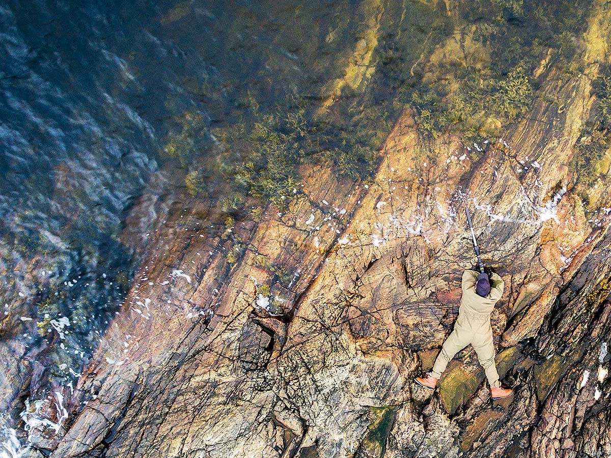 jeger liggende på svaberg sett ovenfra skyter rifle med skytestøtte
