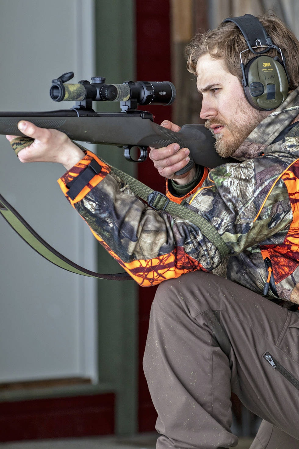 Knestående: Armen din er like lang om du ligger, sitter eller står, så det er ikke behov for å justere den alt etter skytestillingen du bruker. Jeger i sittende jegerstilling sett fra siden sikter med rifle og skytestropp