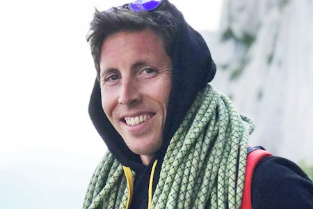 Stian Christophersen. Foto: Tina Johnsen Hafsaas mann med hettegenser ser smilende  inn i kamera med tau rundt halsen og solbriller oppå hodet. bakgrunnen er en fjellvegg