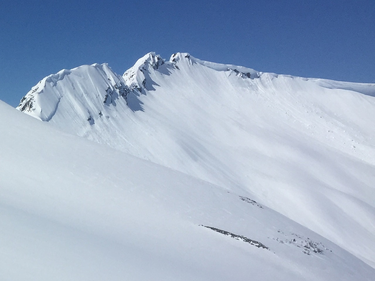 STOR SKREDAKTIVITET: Ryggen mellom Troll- og Åbittind på Nordmøre er nordøstvendt og har en stor skavl som er på vei ned i disse dager. I området ble det observert både løssnø- og flakskred i mange himmelretninger onsdag. Foto: Tore Meirik snøskred topptur