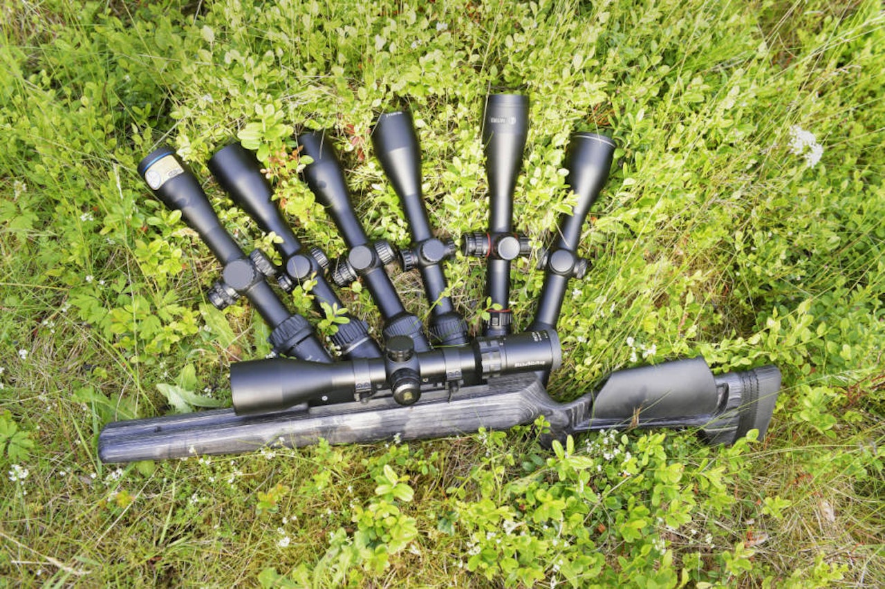 Seks kikkertsikter liggende i gresset og en riflekikkert påmontert riflestokk