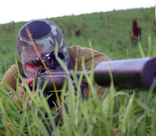 jeger ligger i gresset sikter med rifle