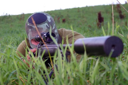 jeger ligger i gresset sikter med rifle