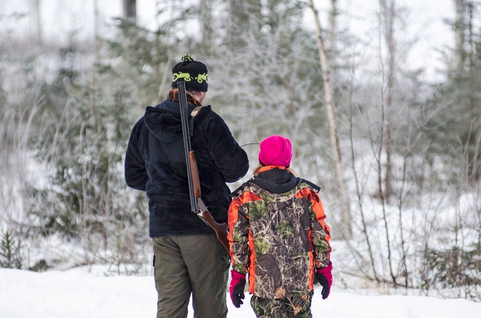 Et barn og en voksen jeger med børse jakter i skogen på vinteren