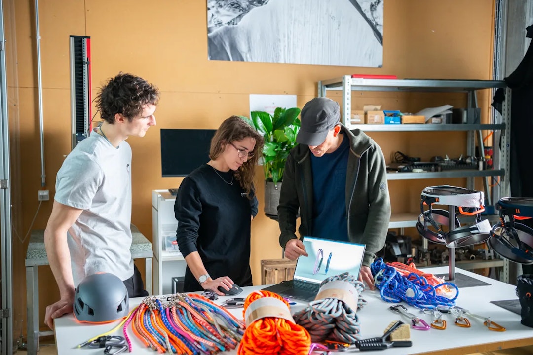 PÅ JOBB: Adam Ondra (til venstre) på et mildt sagt arrangert bilde sammen med folk og utstyr fra Mammut. Foto: Mammut Tre personer ser på klatreutstyr