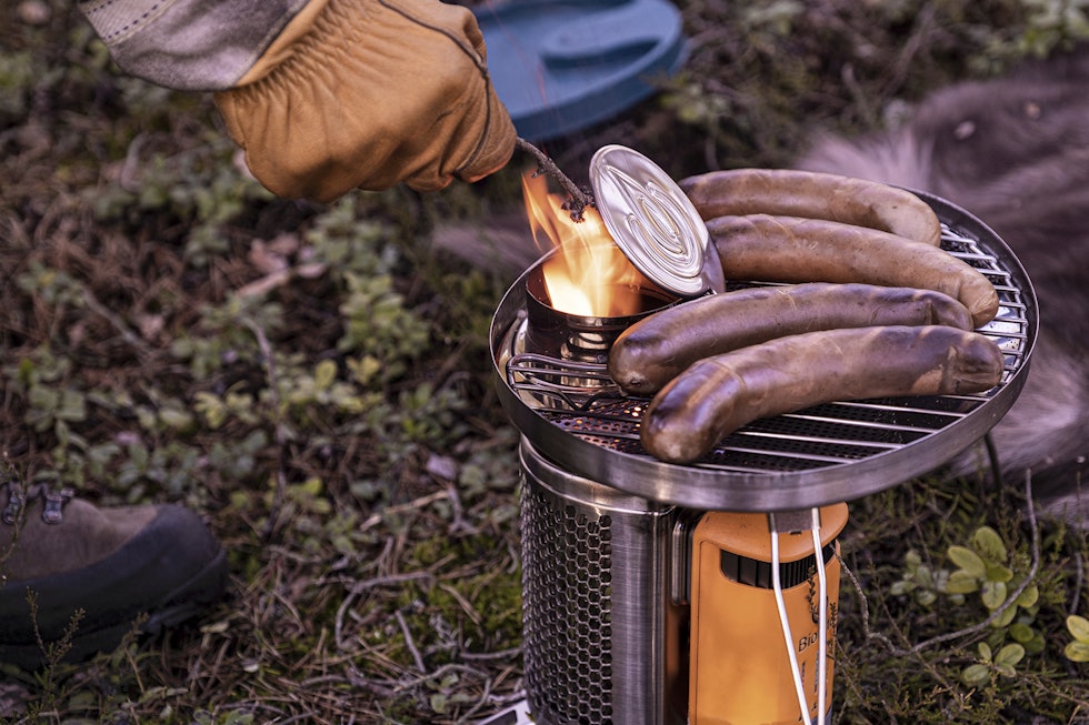 Smart grillhull: Kvistbrenneren kan mates mens grillrista er montert, i motsetning til vannkokeren som må løftes av for alt annet enn småkvist. Bruk hansker, lokket til «brennrøret» blir veldig varmt. Smart grillhull: Kvistbrenneren kan mates mens grillrista er montert, i motsetning til vannkokeren som må løftes av for alt annet enn småkvist. Bruk hansker, lokket til «brennrøret» blir veldig varmt.