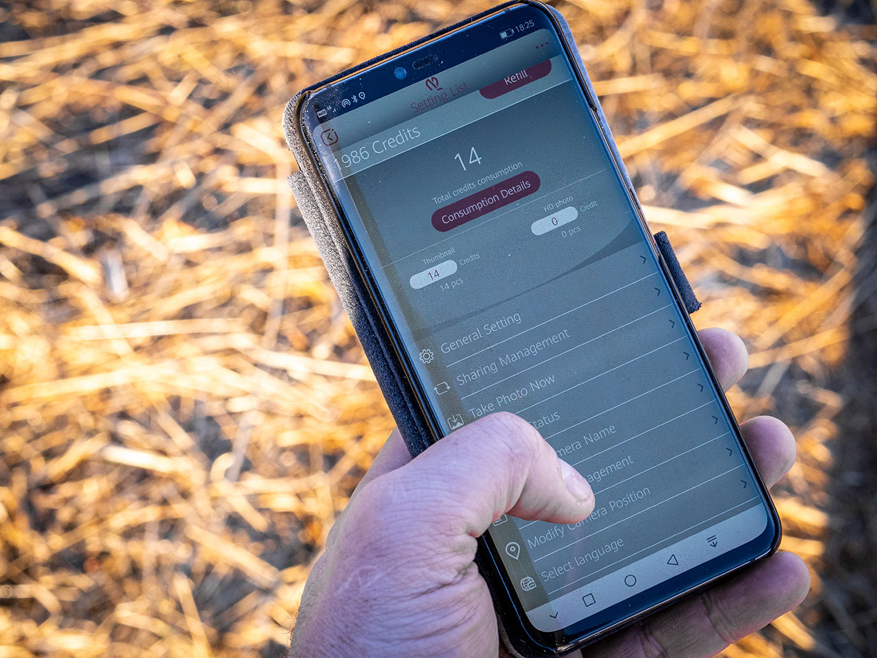 Hånd holder mobiltelefon som styrer viltkamera og app.
