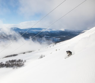 ØKER DAGSKORTPRISEN: Prisen på dagskort for voksne i Oppdal skisenter har økt med over 18 prosent fra forrige til kommende sesong. Foto: Tore Meirik skikjører som svinger med lave skyer og blå himmel bak