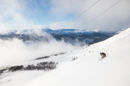 ØKER DAGSKORTPRISEN: Prisen på dagskort for voksne i Oppdal skisenter har økt med over 18 prosent fra forrige til kommende sesong. Foto: Tore Meirik skikjører som svinger med lave skyer og blå himmel bak