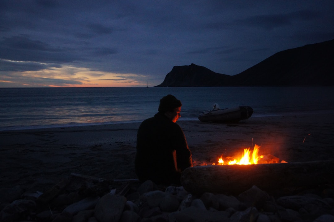 KVALITETSTID: Nils koser seg i skjæret av bålet. Kinnarodden i bakgrunn, Norges nordligste fastlandspunkt. FOTO: Kjell-Harald Myrseth bål strand