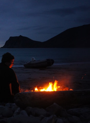 KVALITETSTID: Nils koser seg i skjæret av bålet. Kinnarodden i bakgrunn, Norges nordligste fastlandspunkt. FOTO: Kjell-Harald Myrseth bål strand