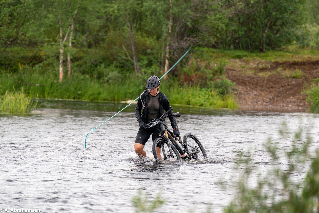 SUPERRITT: Offroad Finnmark er godt i gang og noen av deltakerne har bestemt seg for å prøve å sykle 1150 kilometer på terrengsykkel. Foto: Anders H. Abrahamsen Bærer sykkel over vannet på Offroad Finnmark