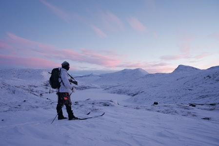 Godt kledd jeger i vinterfjellet med ski, sekk og rifle