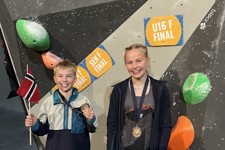 Trym Raum Eide og Johanne Flemmen Bø. Foto. Lars Arne Bø Gutt med norsk flagg og jente, begge smilende med gullmedalje foran innendørs klatrevegg