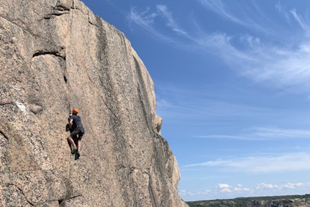 En elev av Petter Åsander på ruten H.D. Evoultion på Skyggeberget (Sotenäs) i Bohuslän. Foto: Petter Åsander mann klatrer sva med blå himmel og sjø i bakgrunnen.
