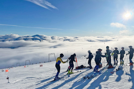 Eierne av Galdhøpiggen Sommerskisenter er mer optimistiske med tanke på hvor lenge de kan drifte enn de var. Foto: Juvasshytta. flere skikjørere i toppen av av bakken. heisanlegg i bakgrunnen