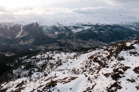 Påskeforholdene mange steder i landet kan by på utfordringer for redningsaksjoner uten helikopter. Foto: Sebastian Jacobsen Et oversiktsbilde over fjell i sogndal med snø mot toppene og bar bakke nærmere dalen.