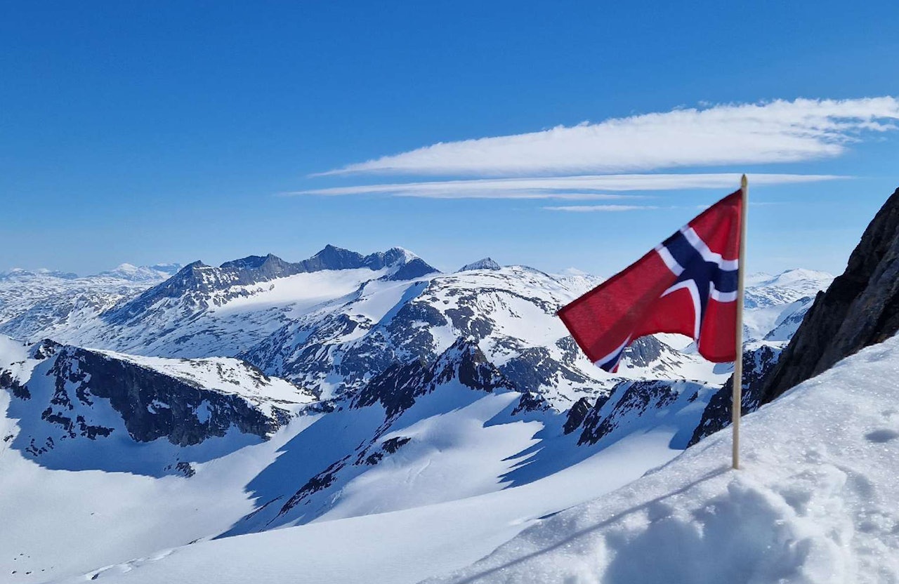 TOPPTUR PÅ NASJONALDAGEN: Lørdag må du stålsette deg for bilder av folk på skitur med både bunad og flagg. Dette er en regobs fra Ofoten på nasjonaldagen i 2024. Foto: turid@nve/regobs norsk flagg i snøkledde fjell