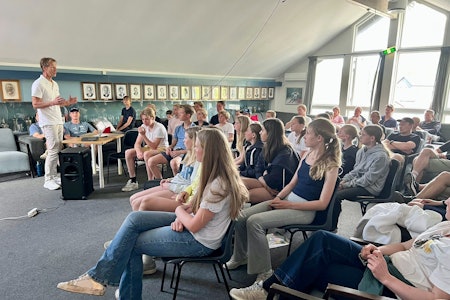 BRASS hadde sitt første skredkurs i Norge for unge alpinister i Bærum. Foto: Norges Skiforbund En mann i hvitt tøy står foran en forsamling av ungdommer i et klubbhus.