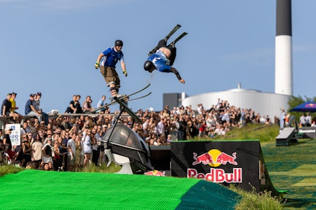 I jibbekonkurransen kjører deltagerne fra hvert land samtidig ned bakken. Foto: Jesper Gronnemark. En mann henger opp ned i luften i et hopp, mens en annen sklir langs toppen av en rail i sommerværet.