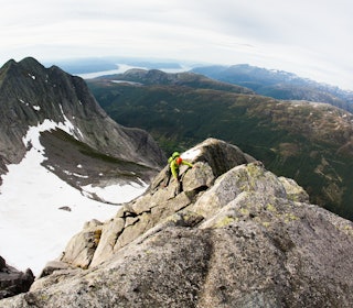 UTSIKT: Brendan Leonard på Kolkjerreryggen (4) i Uskedalen, en ryggtravers opp nordøstryggen på Akslo. Foto: Forest Woodward mann klyver oppover ryggtravers med utsikt over fjord og fjell i bakgrunn