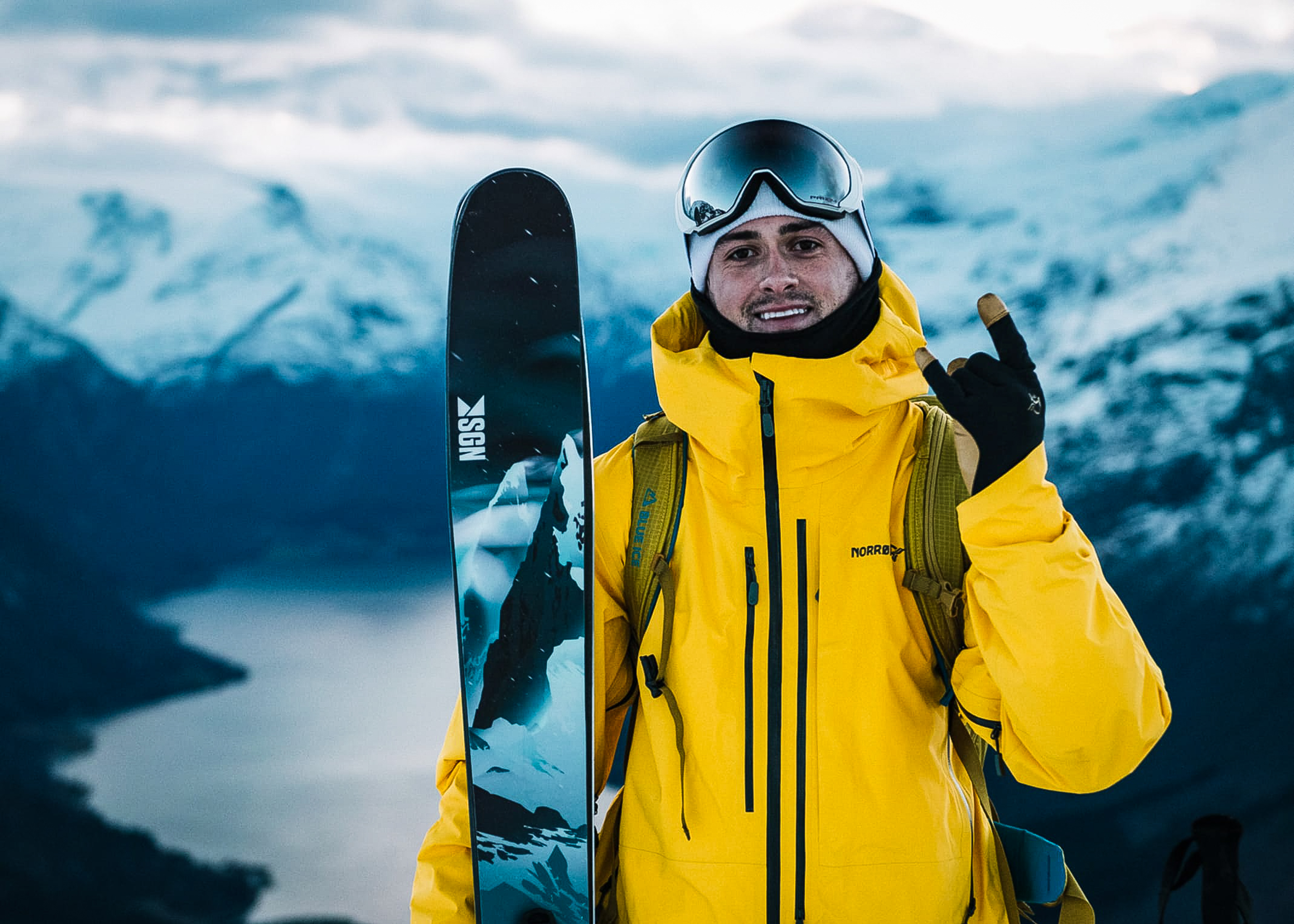 Mannlig skikjører smiler med skiene i hånda og fjellene i bakgrunnen