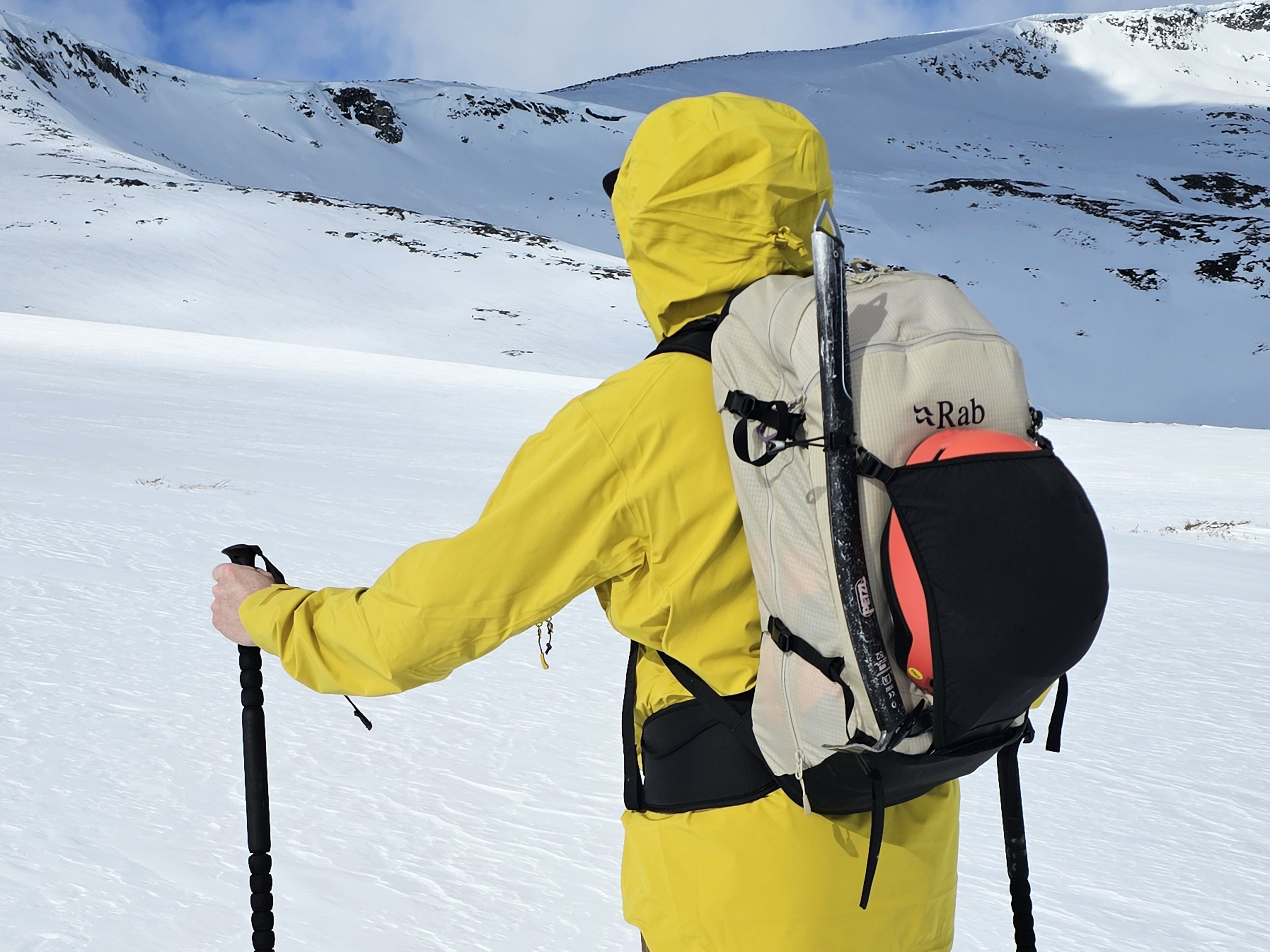 mann med gul jakke og sekk som ser på fjell